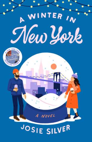 ID: Book cover of A Winter In New York by Josie Silver. Background is blue with snowflakes falling. All white text along with a blue & white snowglobe with a couple in front. 