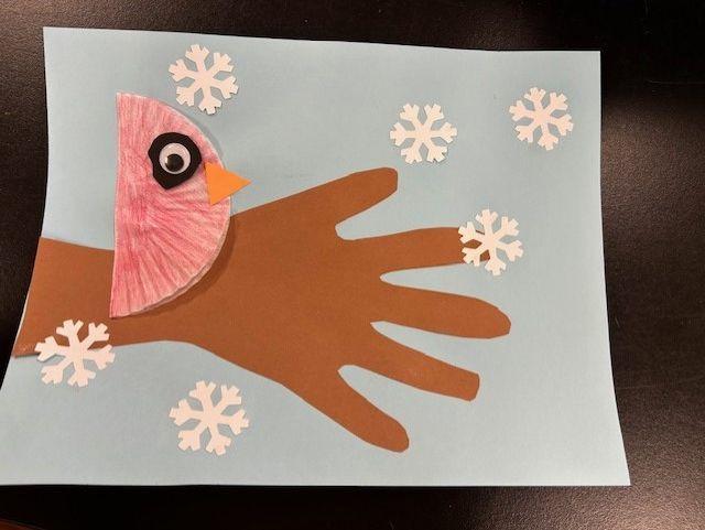 Example craft of red cupcake liner cardinal on a traced cut-out of arm and hand to make a tree branch with snowflakes on a blue background